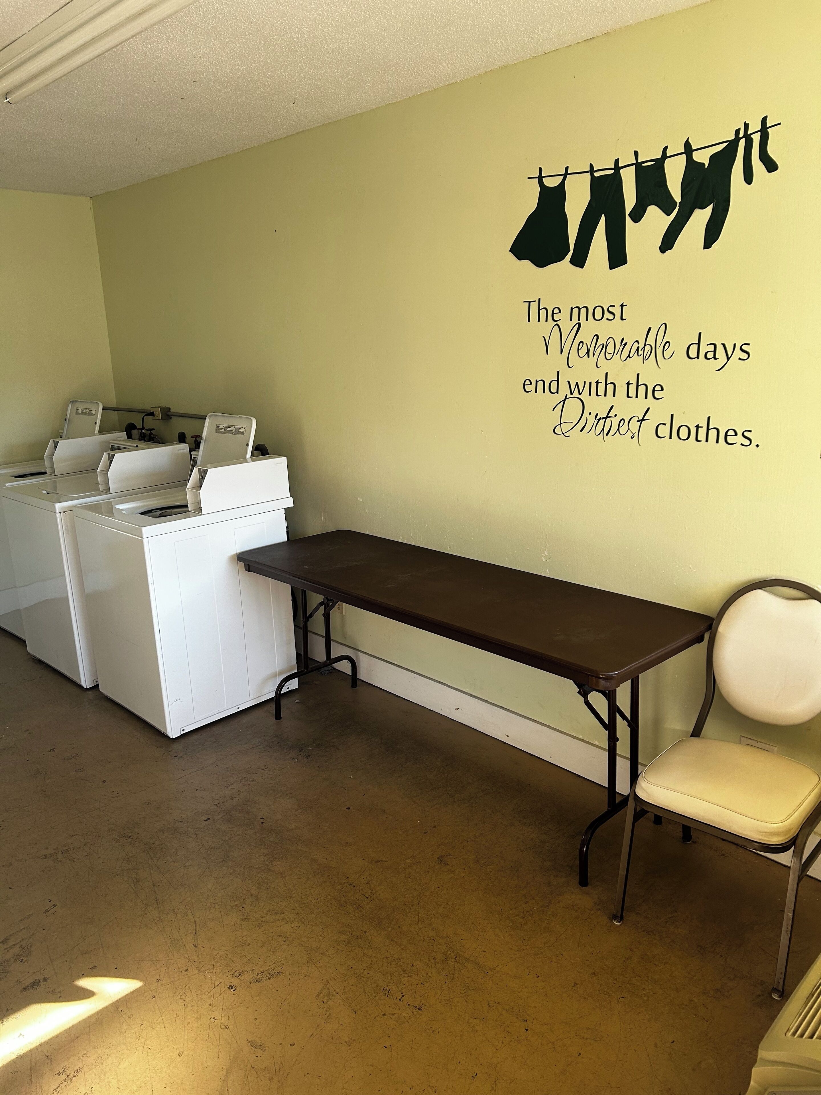 A laundry room with a table and chairs, a wall-mounted drying rack, and a wall decal with a quote.