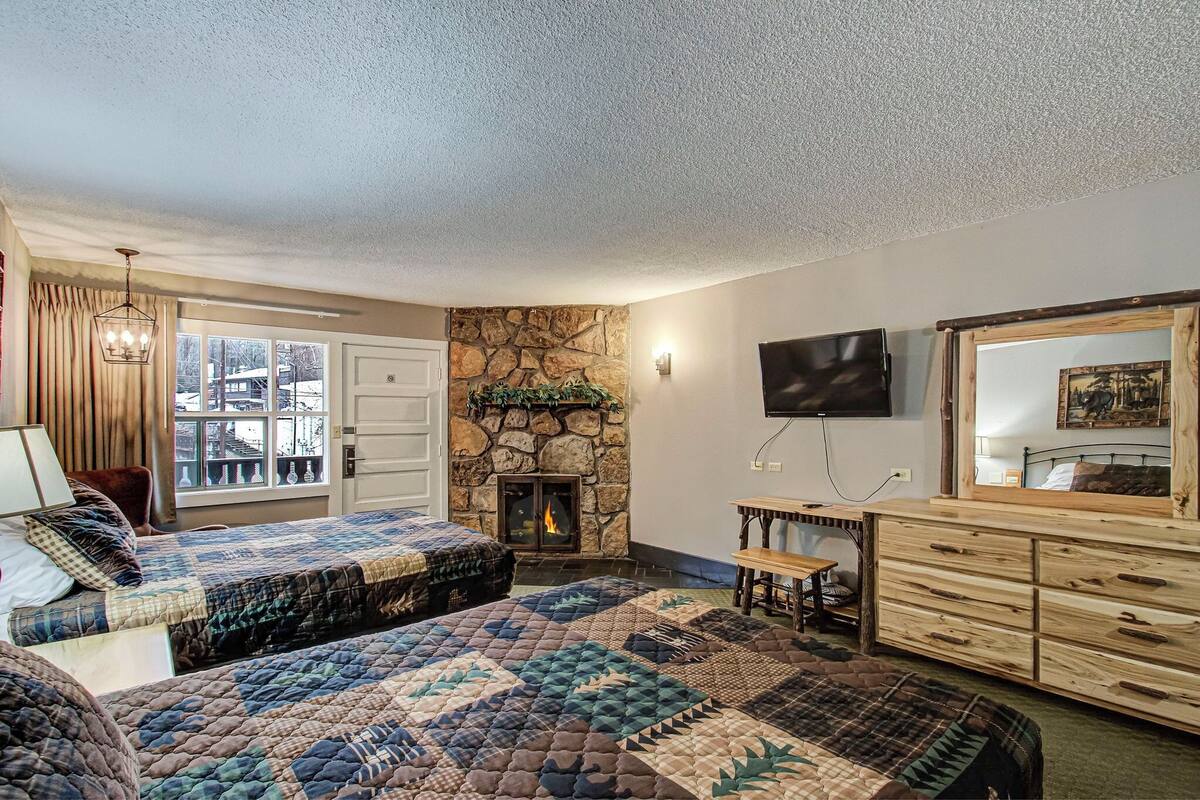 A bedroom with two beds, a stone fireplace, a television, and a large mirror.
