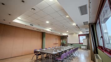 A conference room with a long table, purple chairs, a projector screen, and a window with curtains.