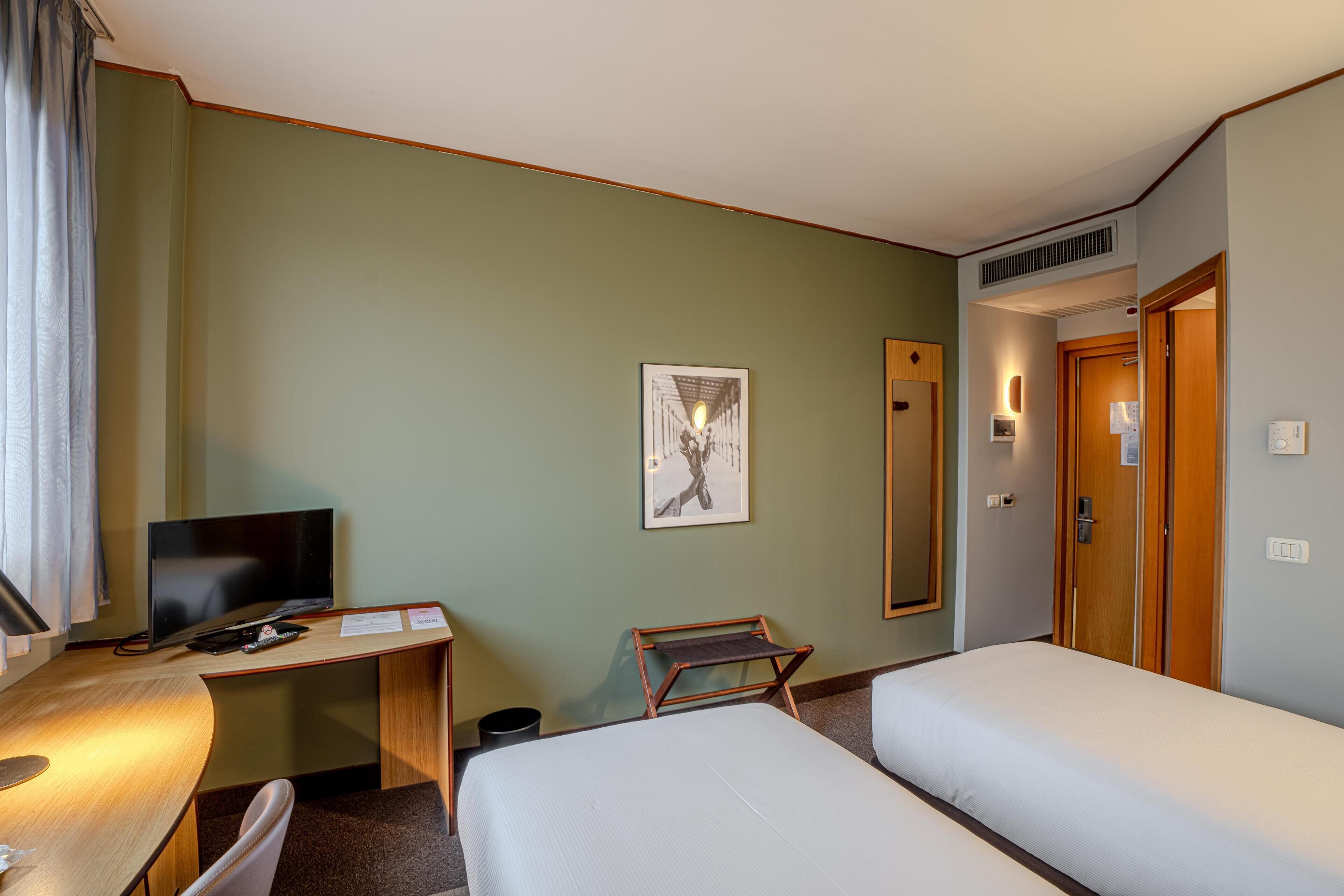 A hotel room with a desk, a television, a bed, and a mirror.