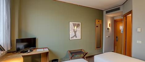 A hotel room with a desk, a television, a bed, and a mirror.