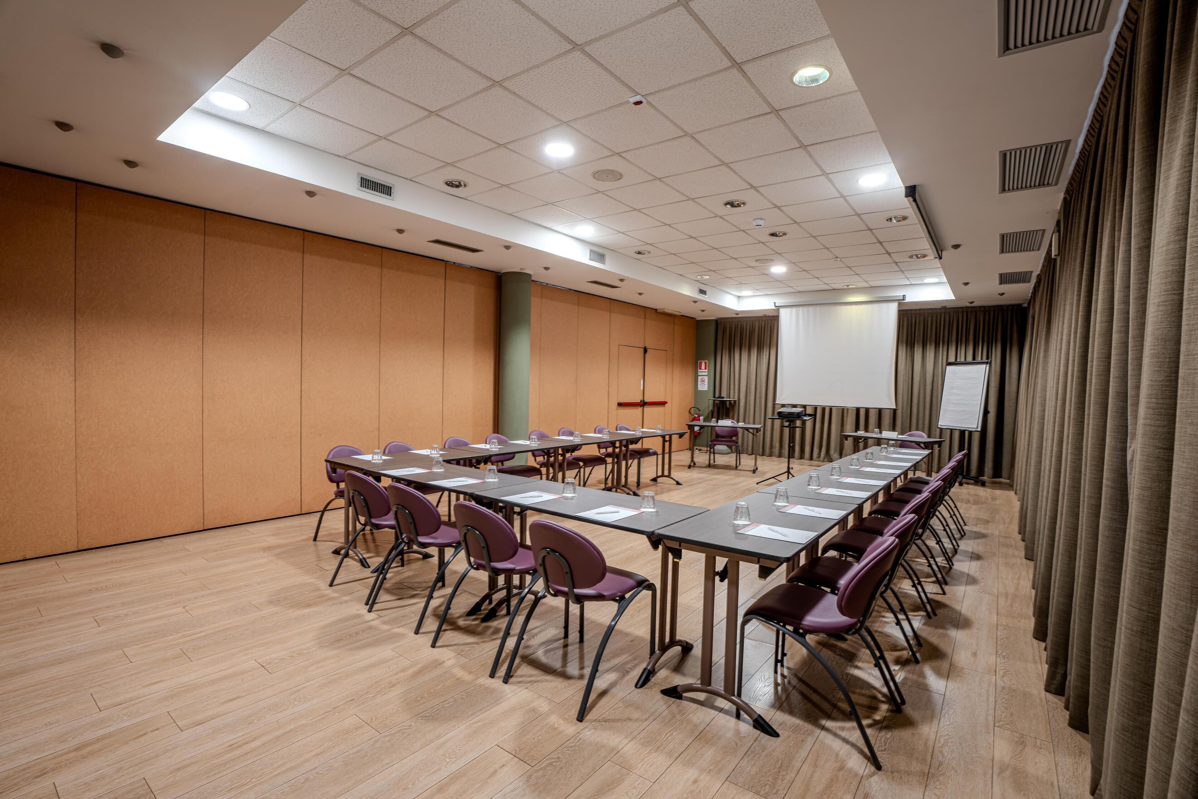 Un salón de conferencias con una larga mesa, sillas, una pantalla de proyector y una pizarra.