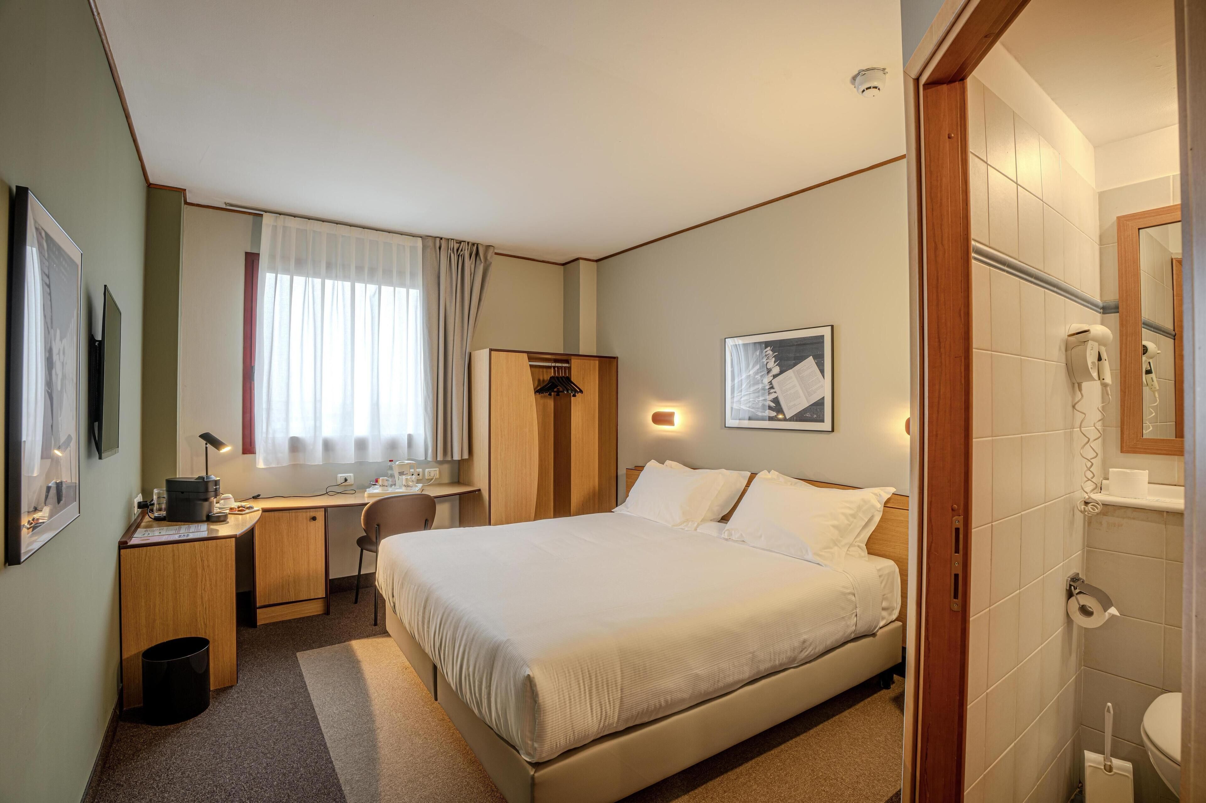 Une chambre d’hôtel avec un lit, un bureau, une chaise et une petite salle de bain.