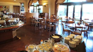 A hotel dining area with multiple tables and chairs, a buffet setup with various food items, and large windows allowing natural light. - Hotel Crown Palais Kokura (Kitakyushu)