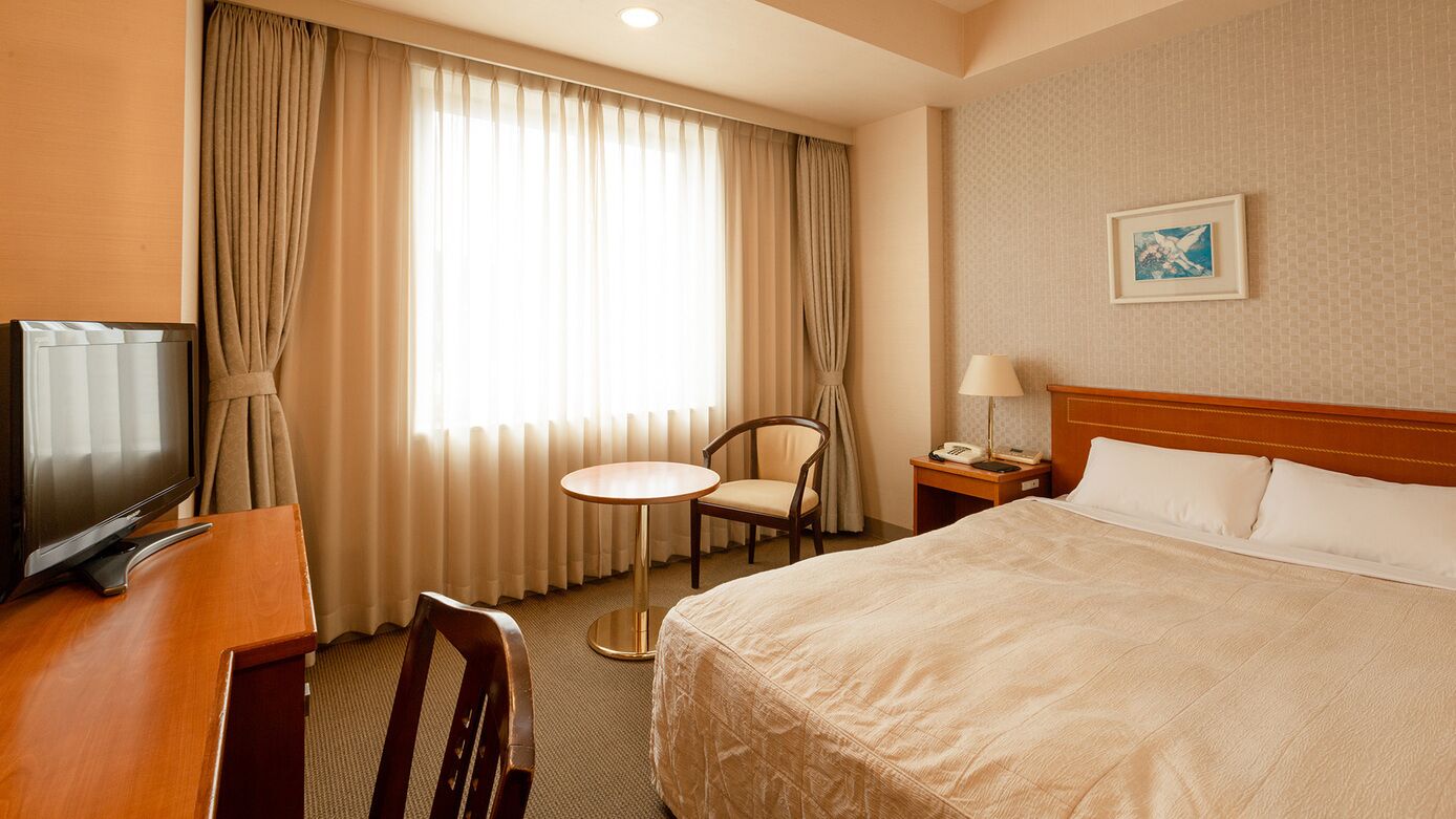 A hotel room with a bed, a desk with a TV, a chair, a small table, a lamp, and a painting on the wall.