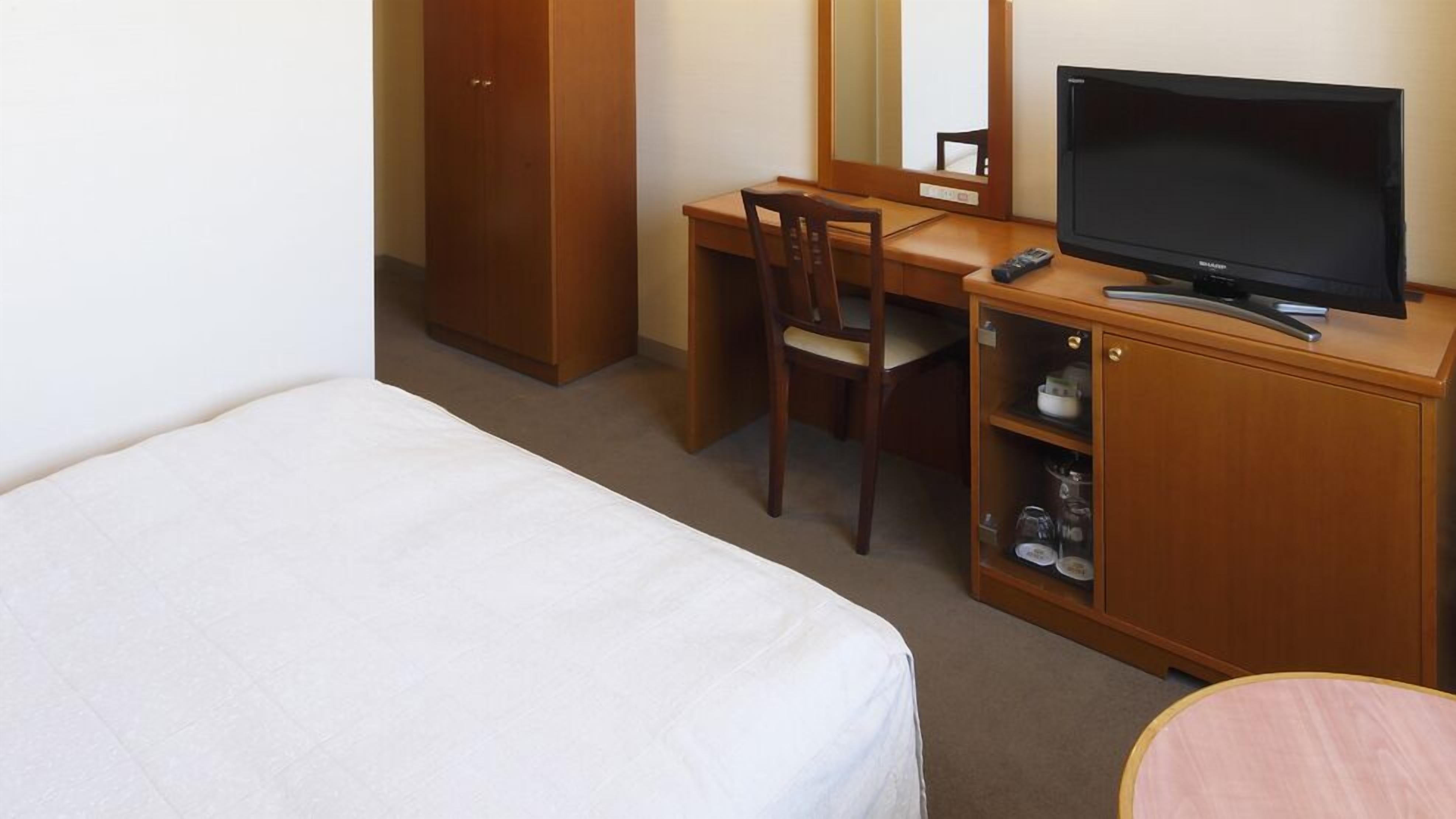 A hotel room with a bed, a desk with a chair, a television, and a cabinet with shelves.