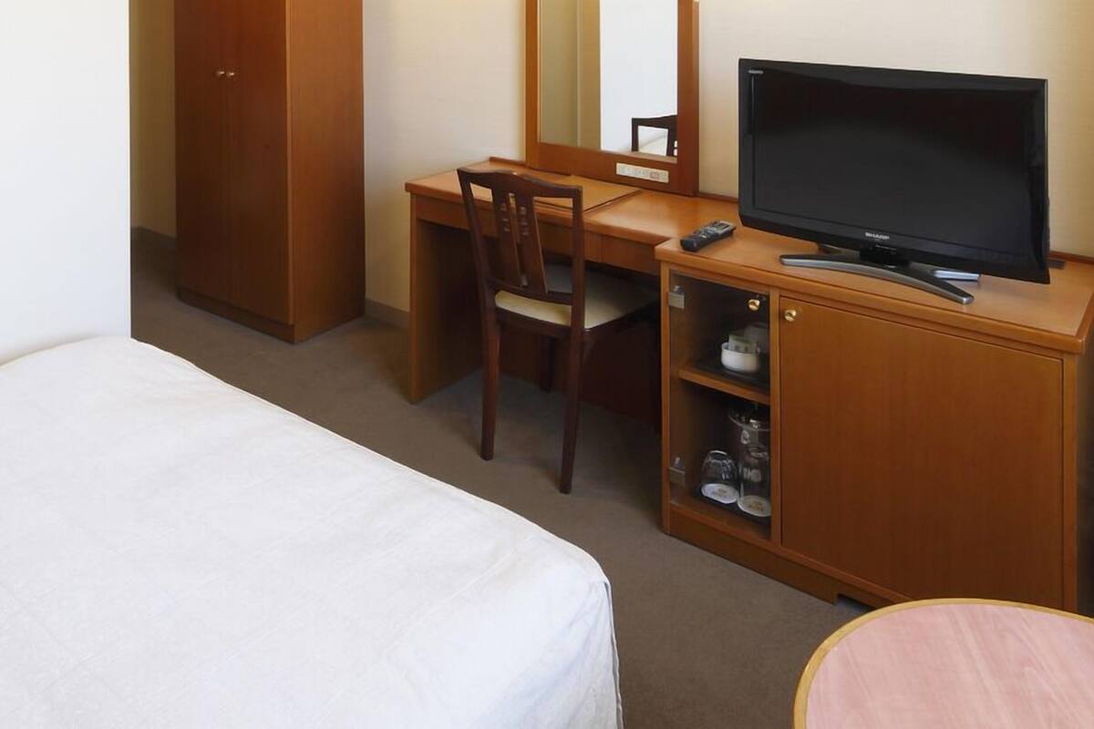 A hotel room with a bed, a desk with a chair, a television, and a cabinet with shelves.