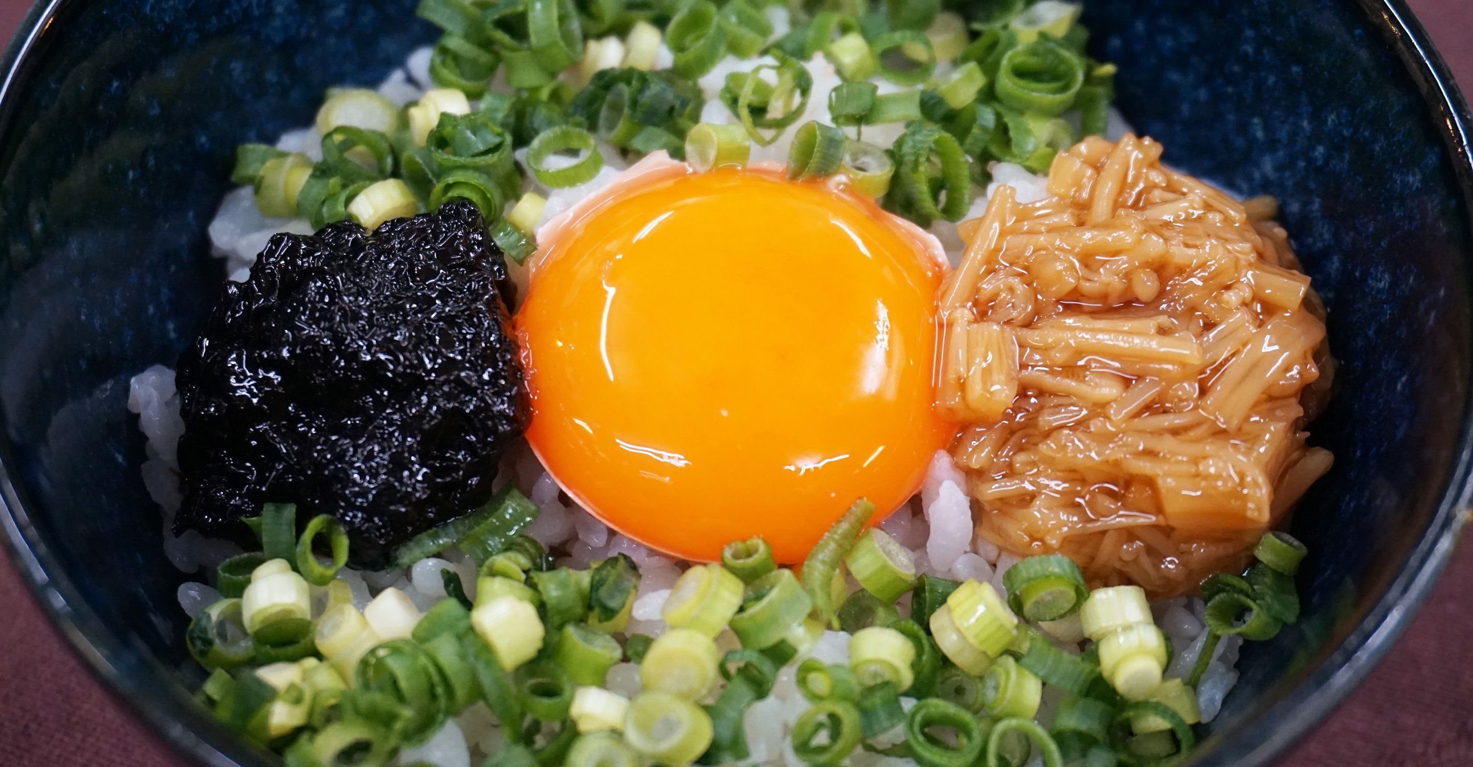 Un bol de riz, un œuf cru et divers accompagnements.