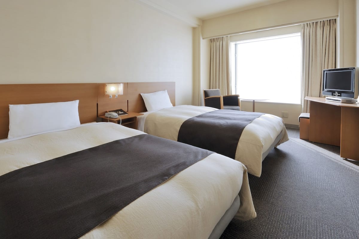 A hotel room with two beds, a desk with a television, and a window with curtains.