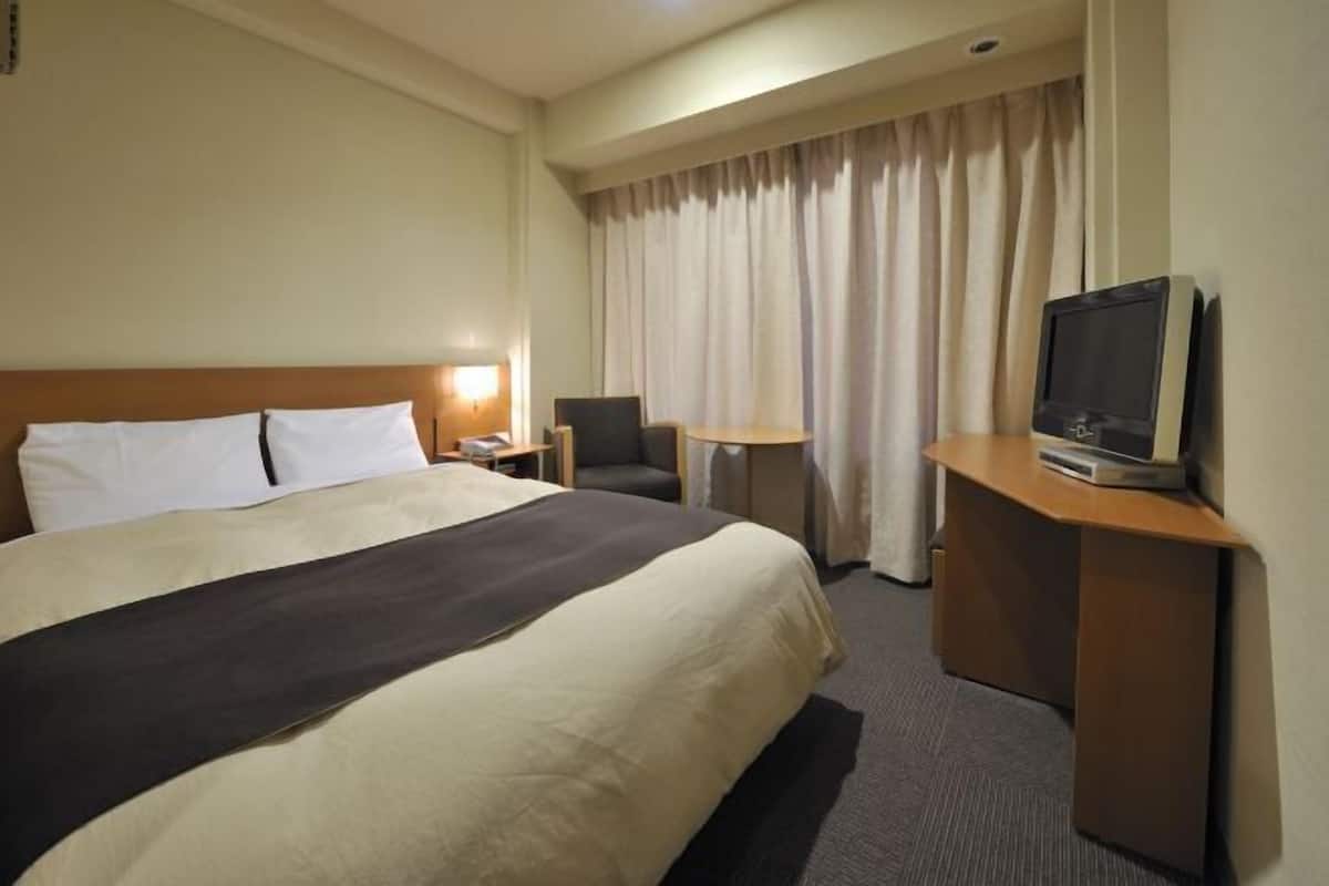 A hotel room with a large bed, a desk with a television, a chair, and a small table.