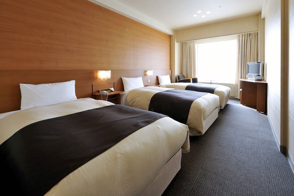 A hotel room with three beds, a television, and a desk with a lamp.