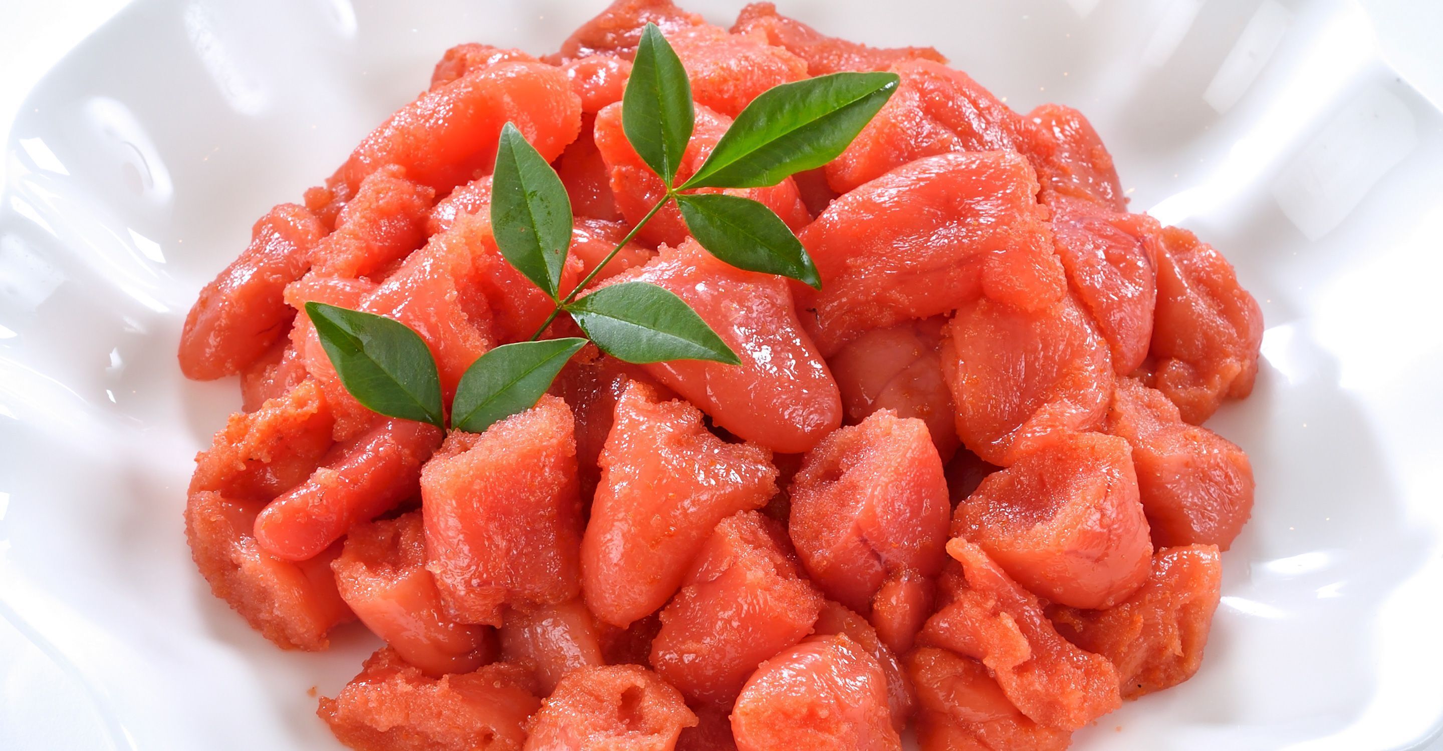 Une assiette blanche contenant des tomates coupées en dés, garnie de feuilles vertes.