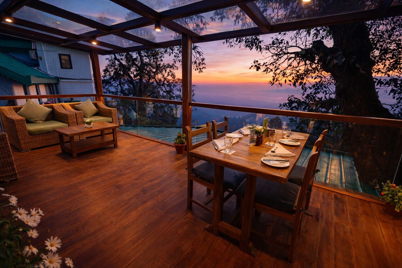 Una terraza de madera con una mesa para dos, sillas de mimbre y vista al atardecer.