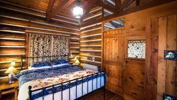 A log cabin bedroom with a bed, wooden walls, a patterned headboard, and a wooden door with a window.