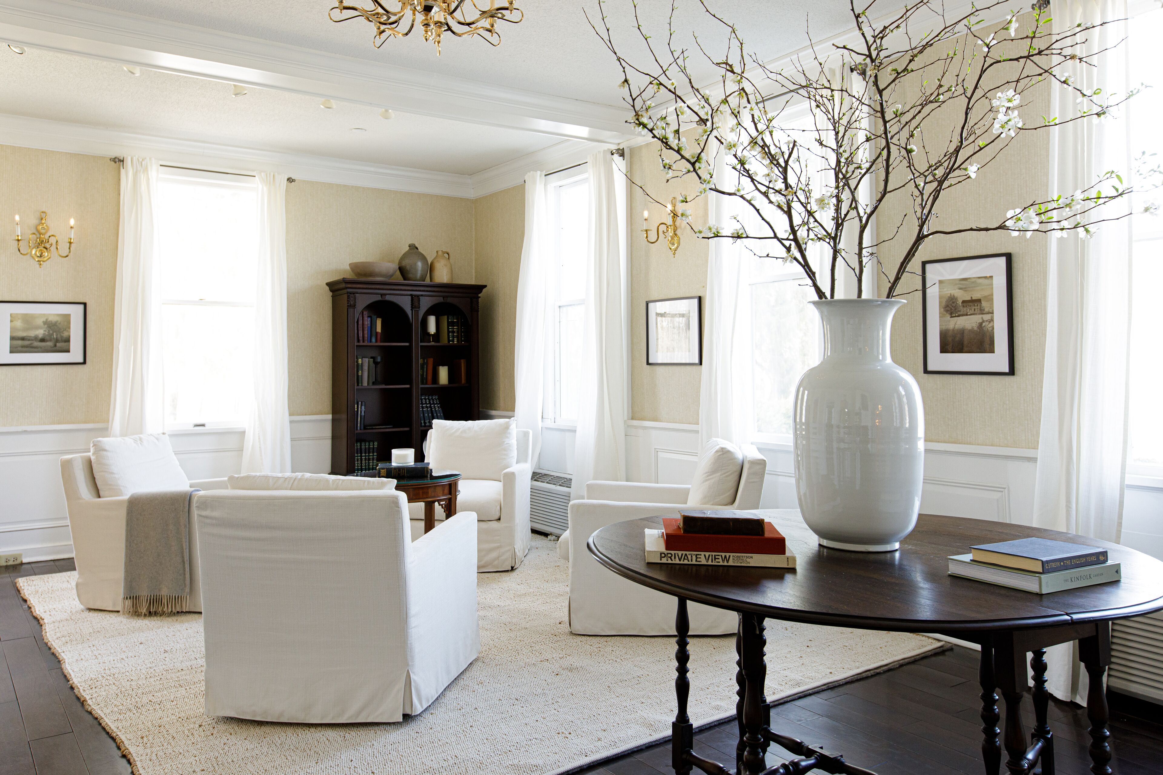 A well-lit living room with a large white vase on a table, surrounded by white furniture and a dark wooden floor.