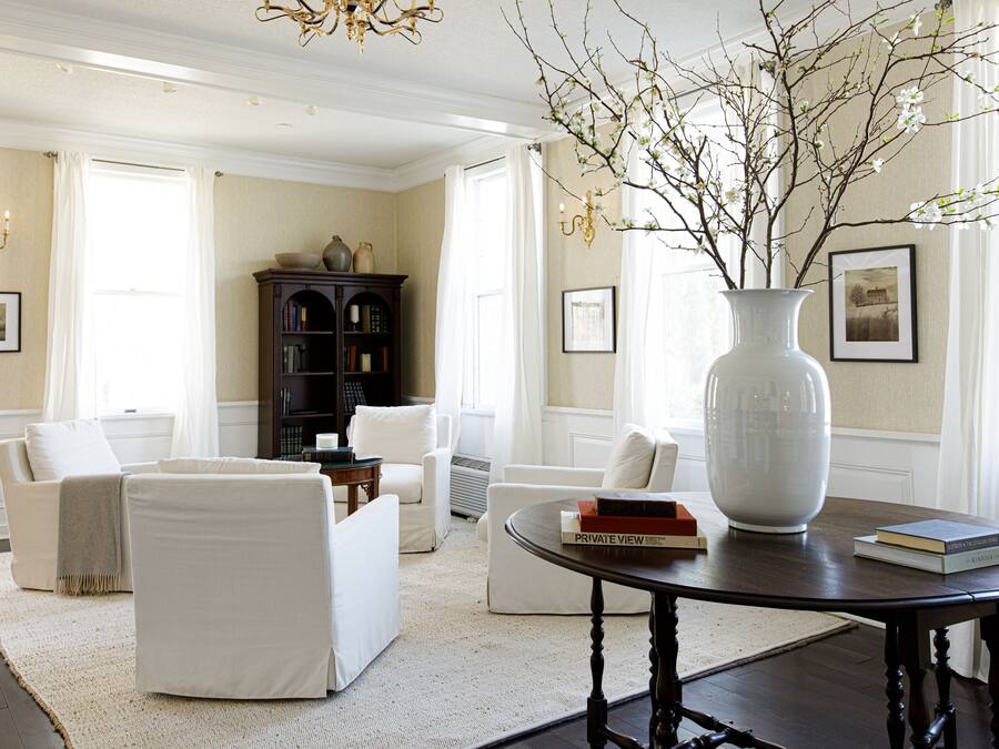 A well-lit living room with a large white vase on a table, surrounded by white furniture and a dark wooden floor.