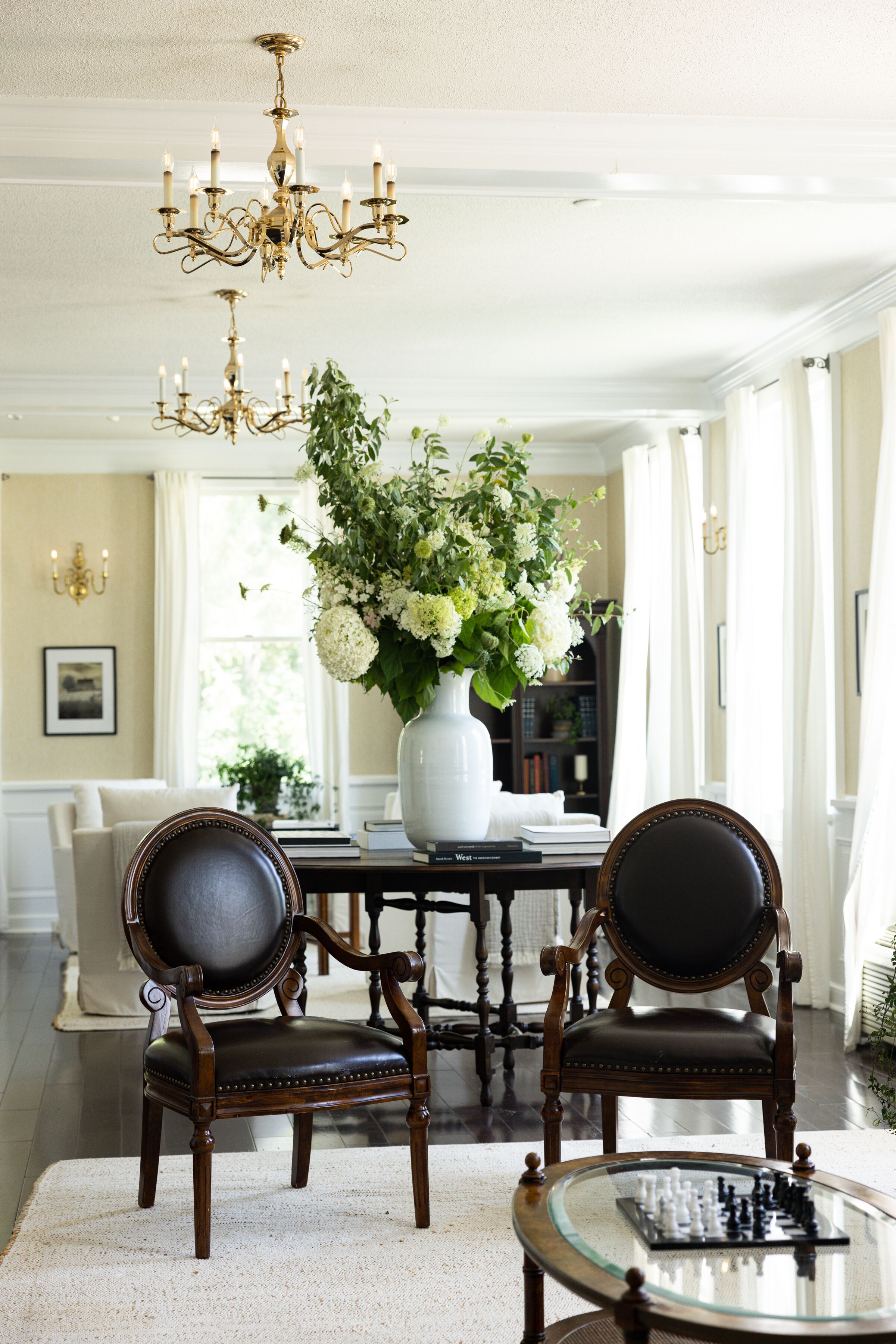 A dining area with a chandelier, a vase of flowers, and two chairs.