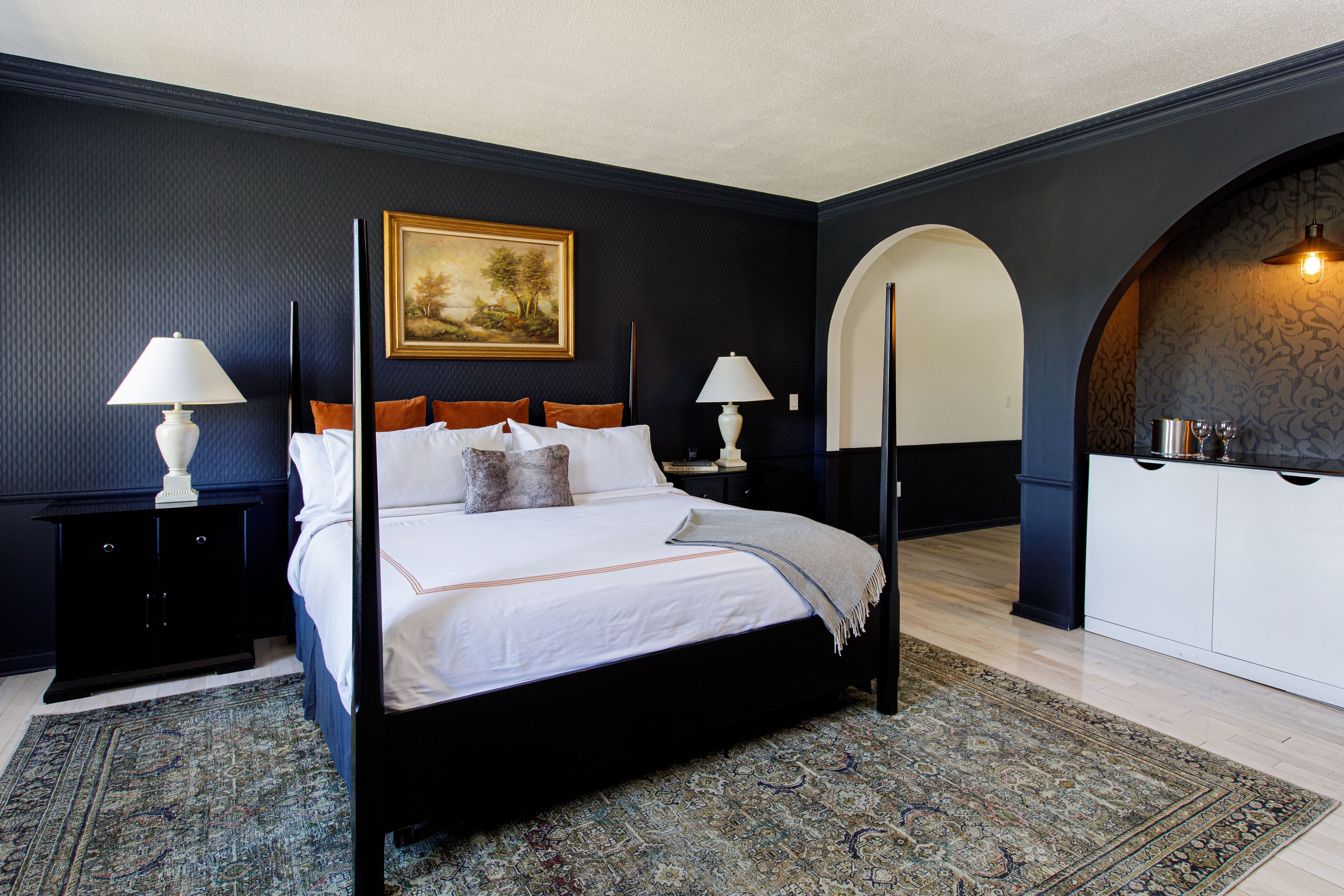 A bedroom with a large bed, two bedside tables with lamps, a painting on the wall, and a wardrobe with a mirror.