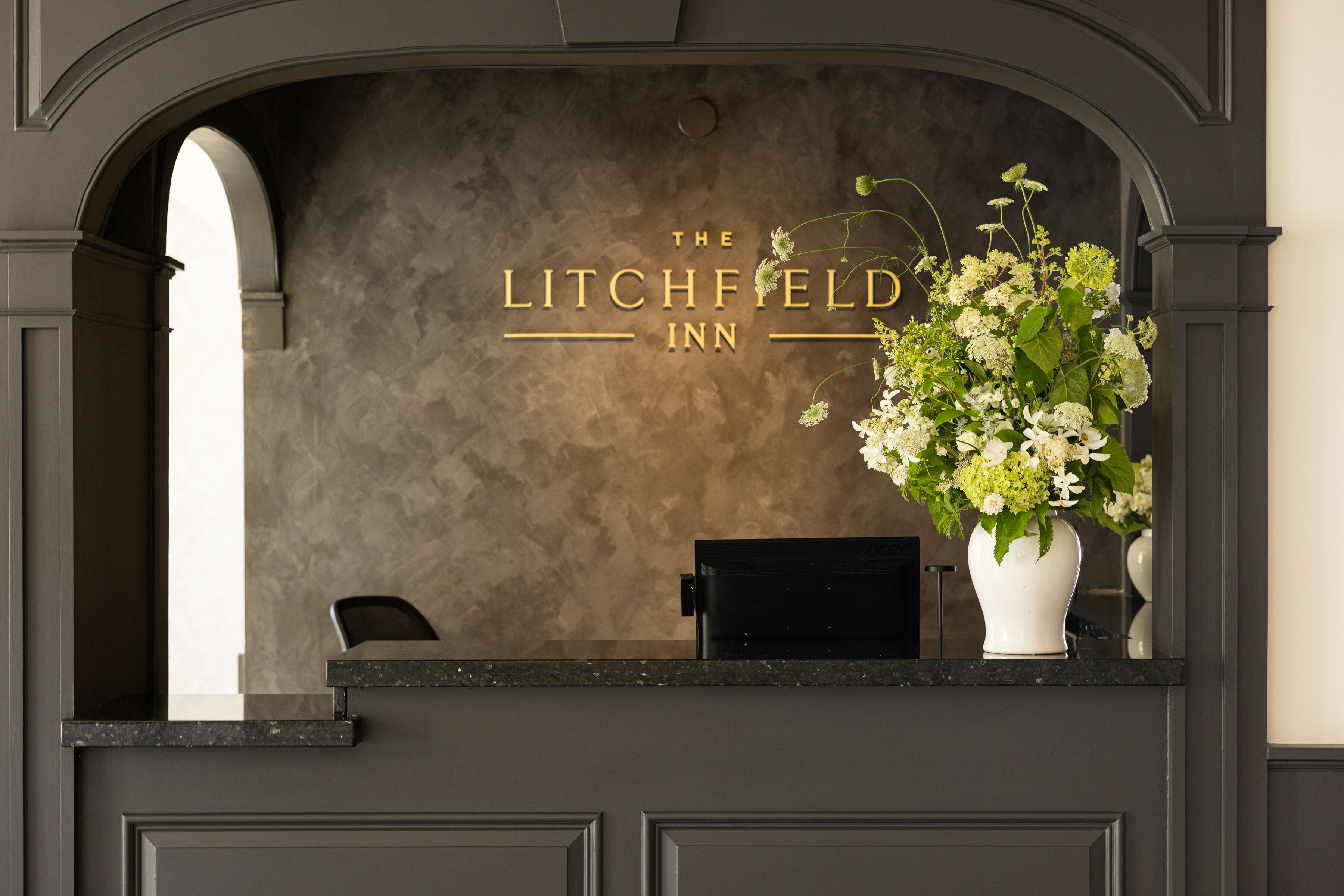Una mesa de recepción con un letrero que dice "The Litchfield Inn" y un jarrón con flores.