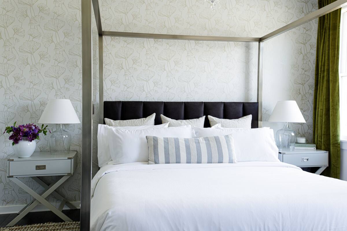 A neatly made bed with white bedding and striped pillows, flanked by two bedside tables with lamps and a vase of flowers.
