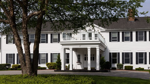 A large, white, two-story building with a central entrance flanked by columns, surrounded by well-maintained greenery.