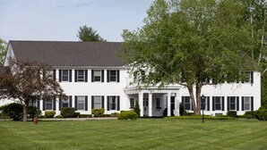 A large, two-story white building with a symmetrical facade, featuring a central entrance with columns, surrounded by well-maintained lawns and mature trees.