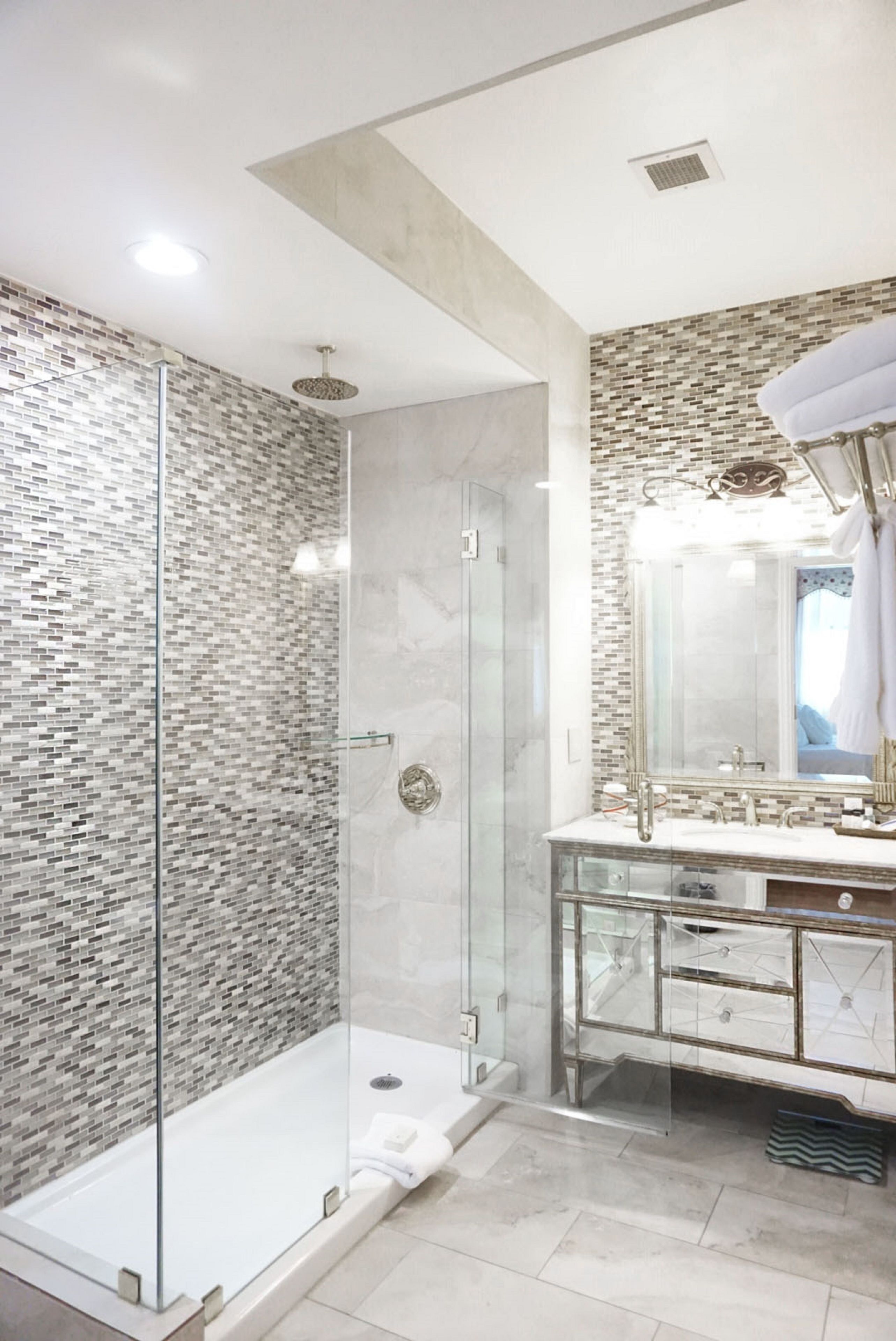 A modern bathroom with a glass-enclosed shower, a large mirror, and a vanity with a tiled backsplash.