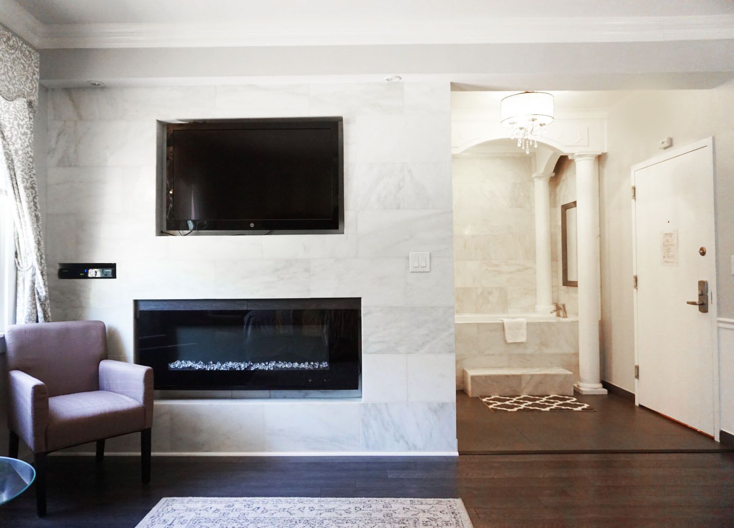 A modern living room with a flat-screen TV mounted above a fireplace, a comfortable armchair, and a patterned rug on the floor.