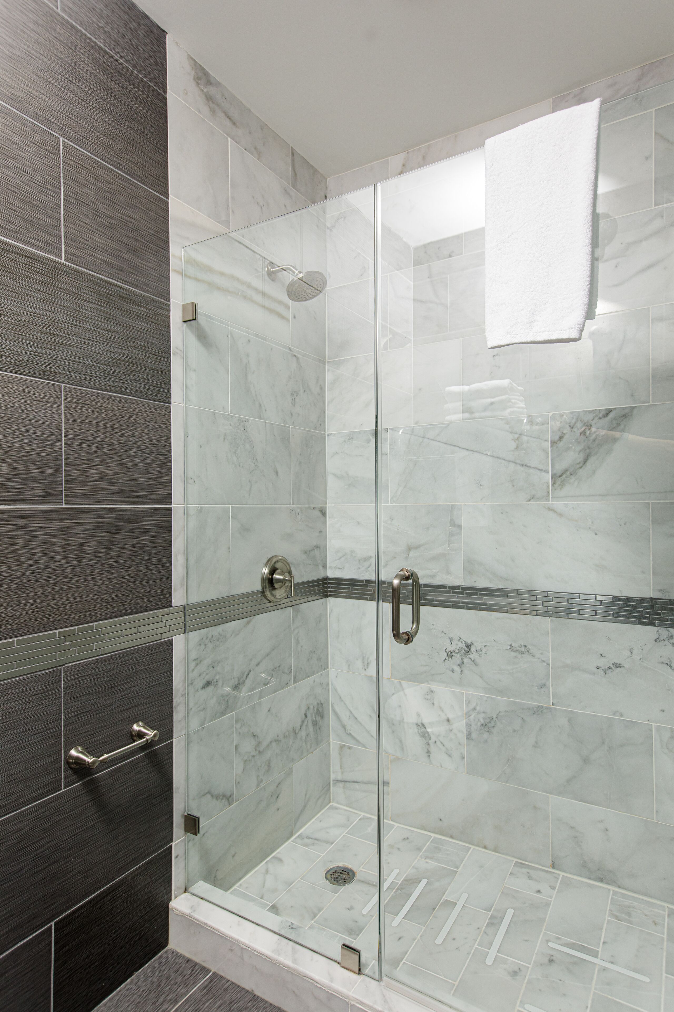 A glass-enclosed shower with a marble tile design and a towel hanging on the door.