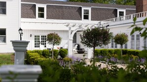A white building with a covered patio area, a brick chimney, and a garden with various plants and flowers. - The Litchfield Inn (Litchfield)