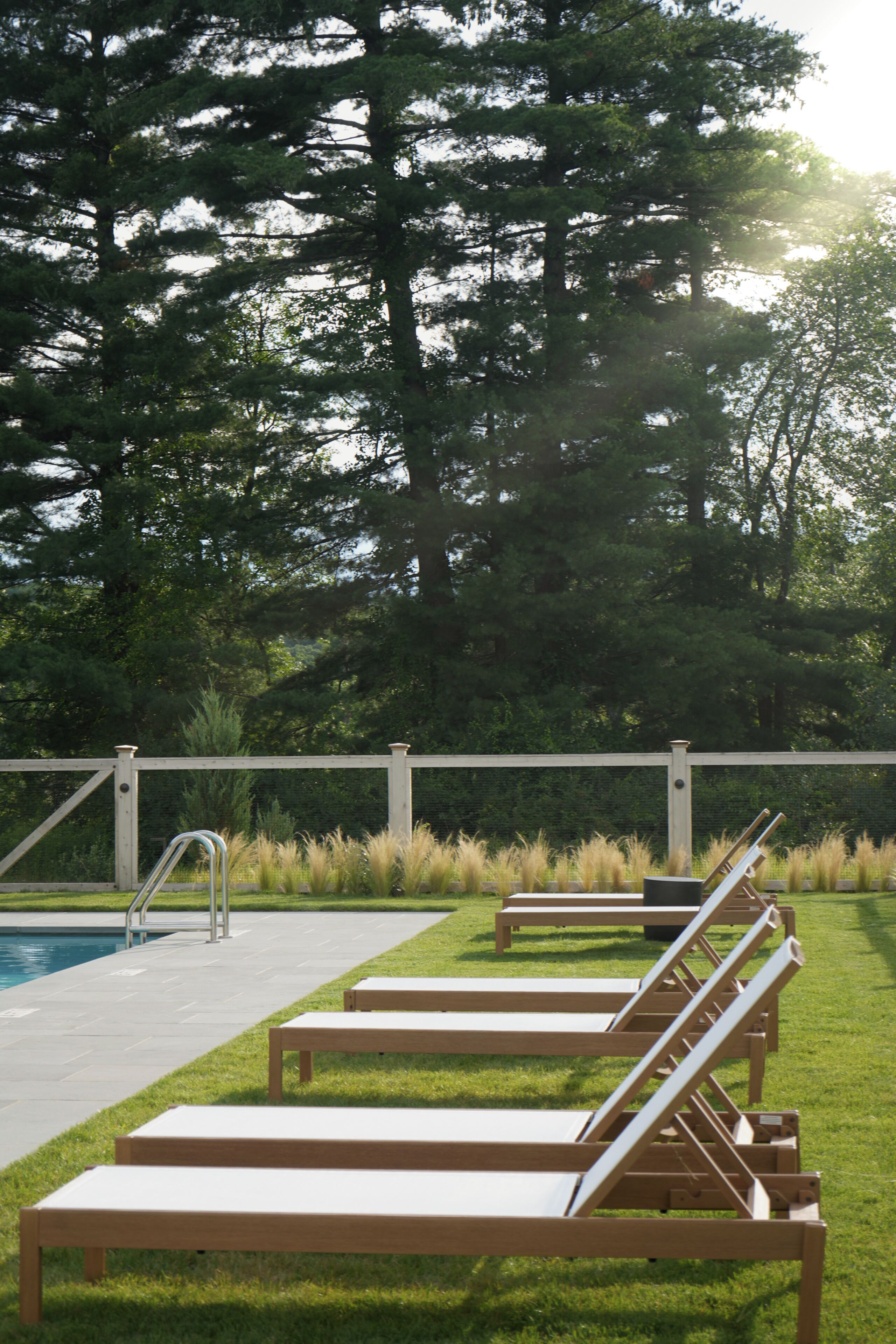 A poolside area with lounge chairs, a pool, and a fence.