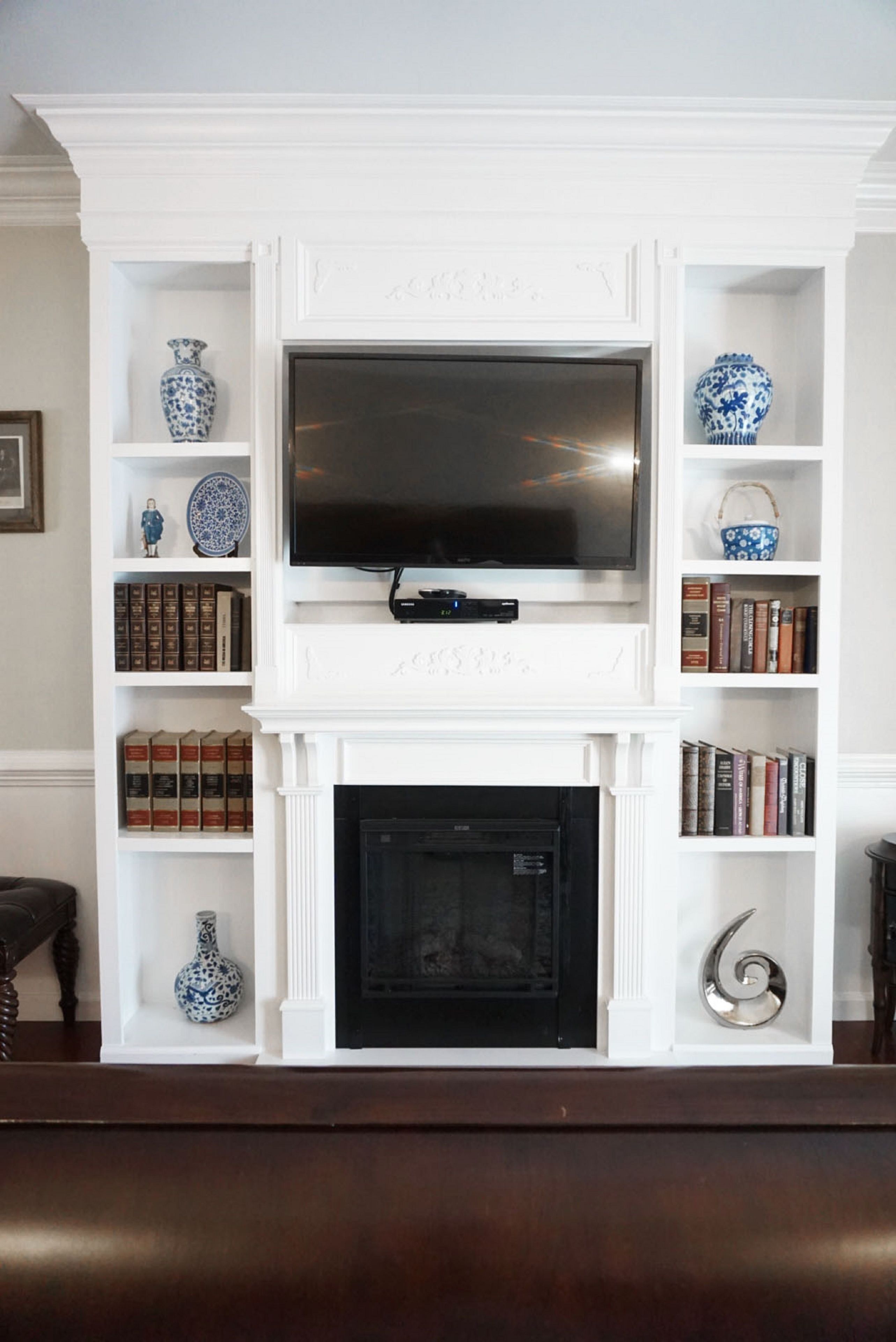 A living room with a fireplace, a flat-screen TV mounted above it, and bookshelves on either side.