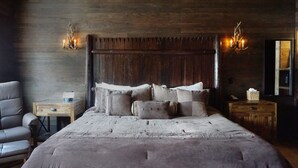 A rustic bedroom with a large bed, wooden headboard, and a wooden floor. There is a chair and a small table with a lamp. - The Litchfield Inn (Litchfield)