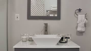 Un baño con un lavamanos blanco, muebles grises, un espejo y un perchero para toallas.