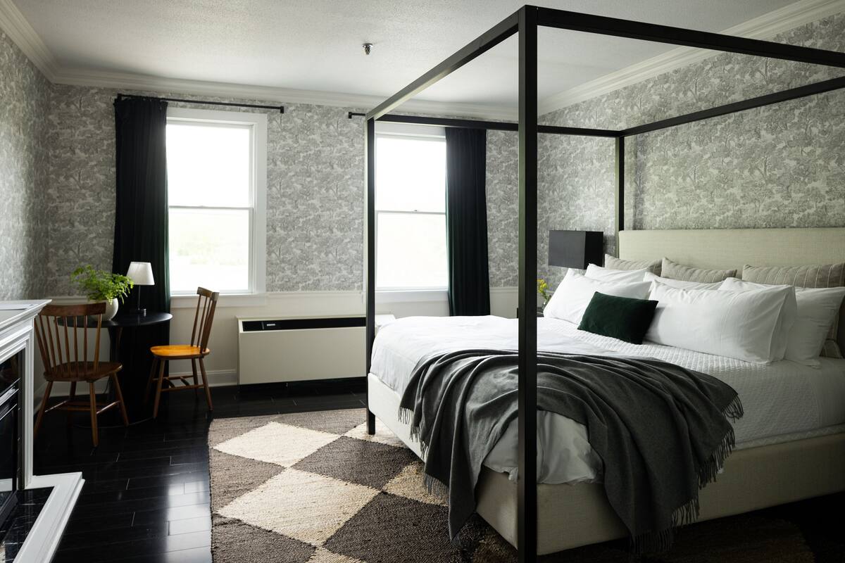 A four-poster bed with a headboard, a desk with a chair, and a window with curtains.