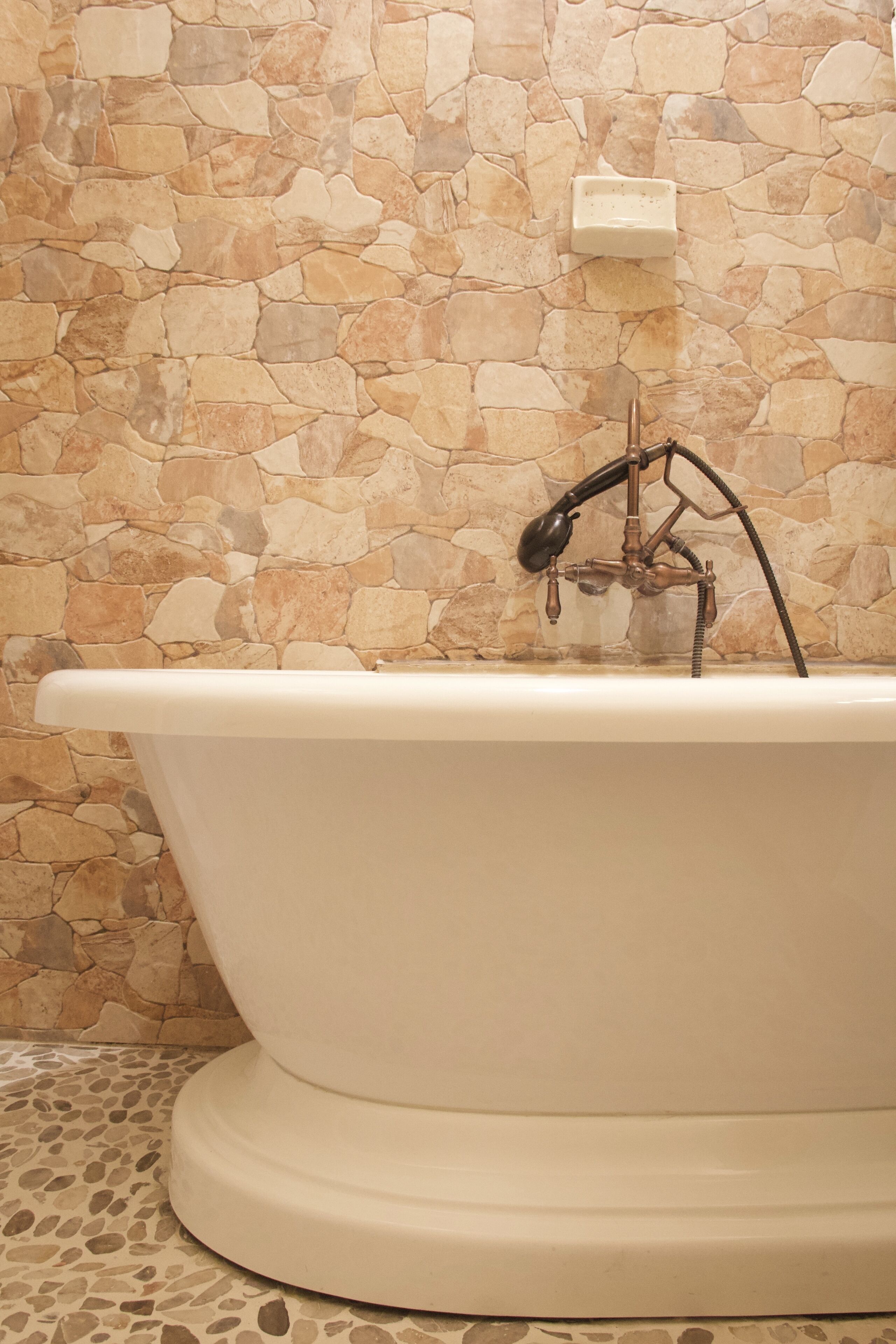 A bathtub with a stone wall backdrop and a marble floor.