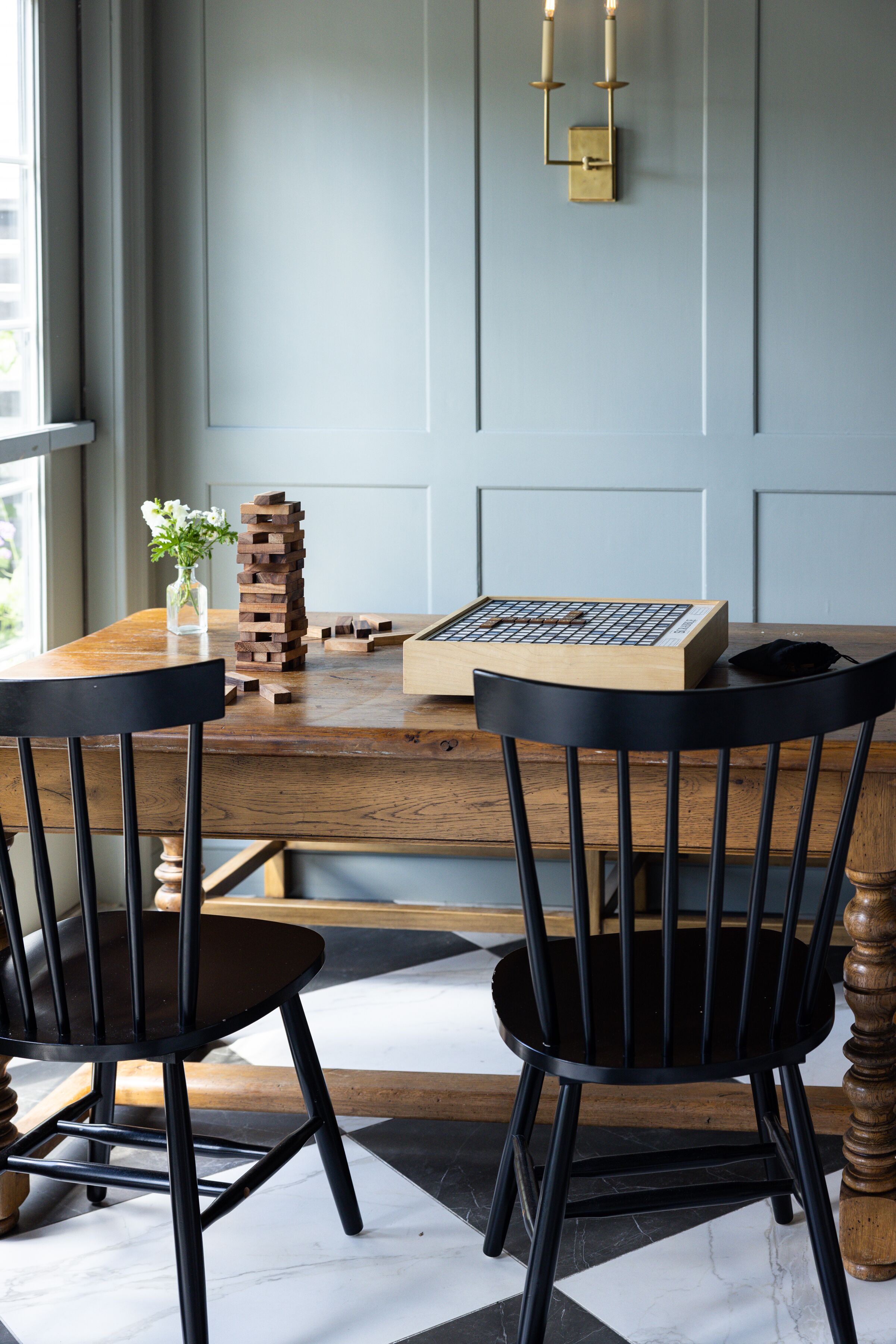 A wooden table with a jigsaw puzzle, two black chairs, and a vase with flowers.