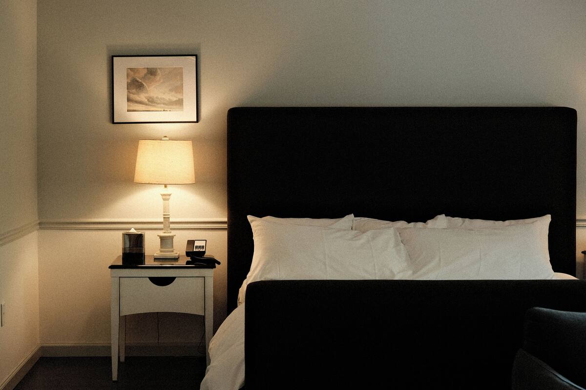 A hotel room with a bed, a nightstand, a lamp, and a framed picture on the wall.