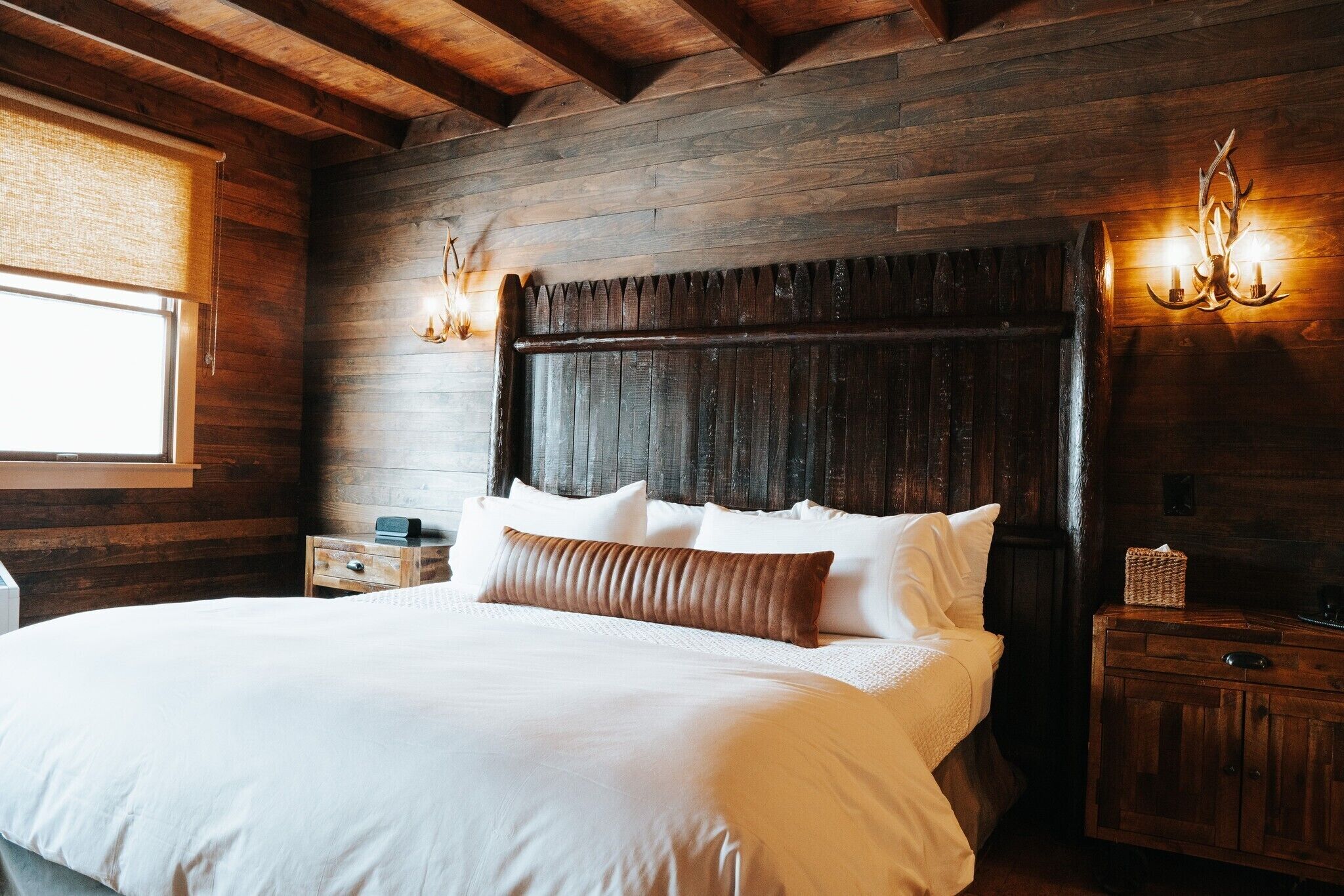 A large bed with white linens and a wooden headboard, flanked by two wall-mounted sconces.