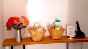 A reception desk with a mirror, a vase of flowers, two woven baskets, a bottle, and two green bottles on the floor.