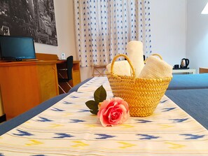 A hotel room with a bed, a desk with a computer, a chair, a basket with towels, and a rose on the bed. - Hostal Ca'n Tiu (Alaro)