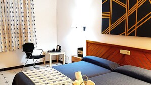 A hotel room with two beds, a desk, a chair, and a wall-mounted light fixture.