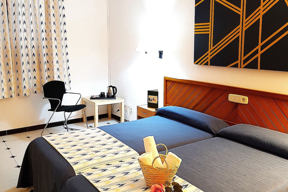 Une chambre d’hôtel avec deux lits, un bureau, une chaise et un luminaire fixé au mur.