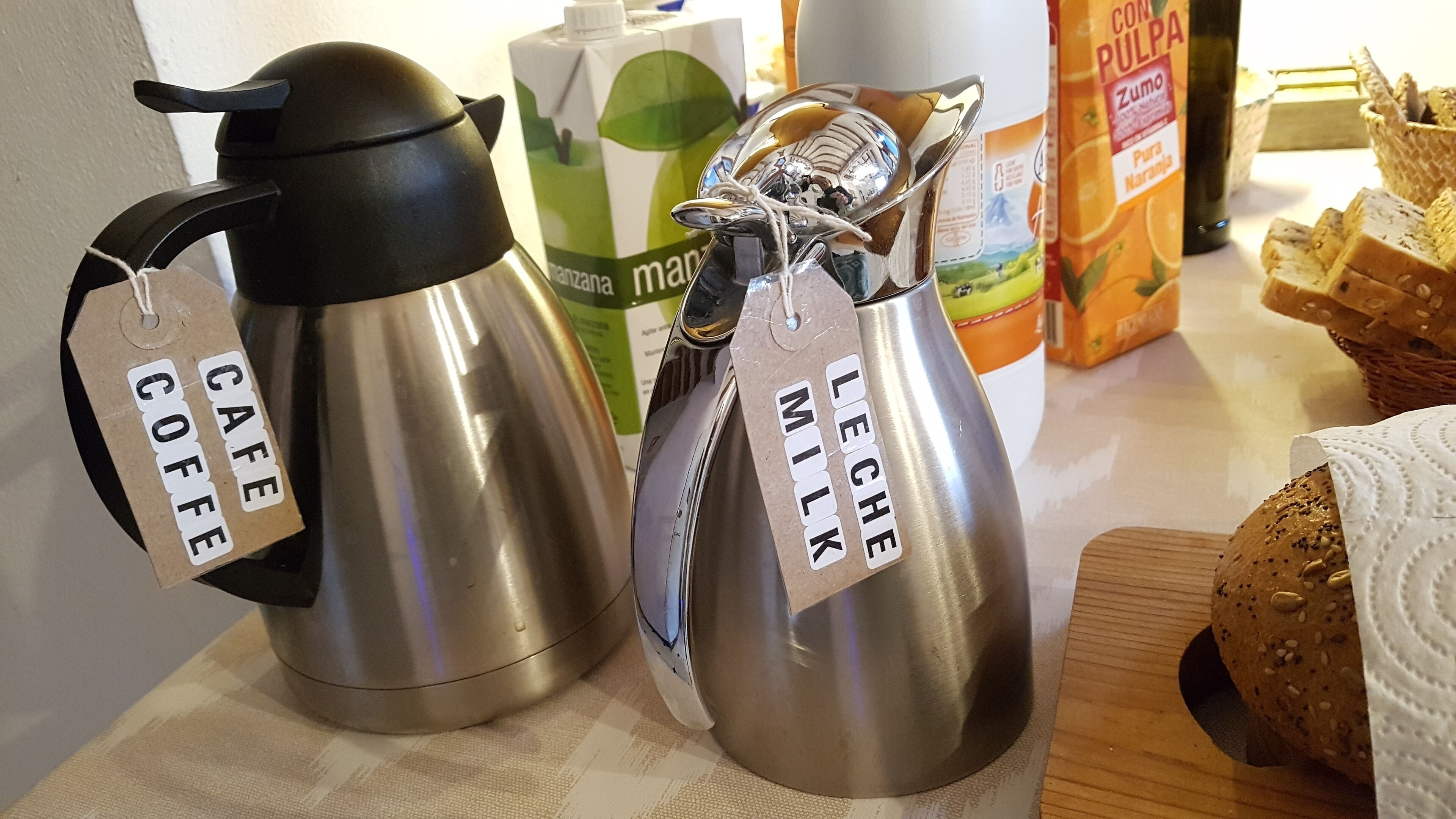 Two stainless steel coffee pots labeled 'Café Coffee' and 'Leche Milk' on a kitchen counter.