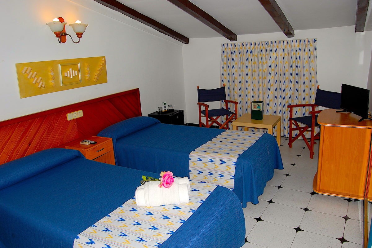 Une chambre d’hôtel avec deux lits, un bureau, une chaise, une télévision et un rideau.