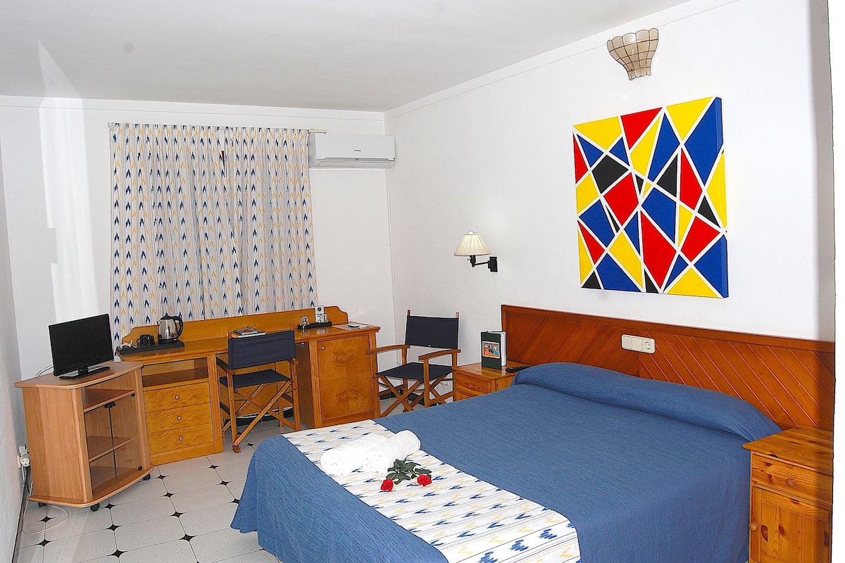 Une chambre d’hôtel comprenant un lit, un bureau avec un ordinateur, une chaise, une télévision et un élément de décoration murale.