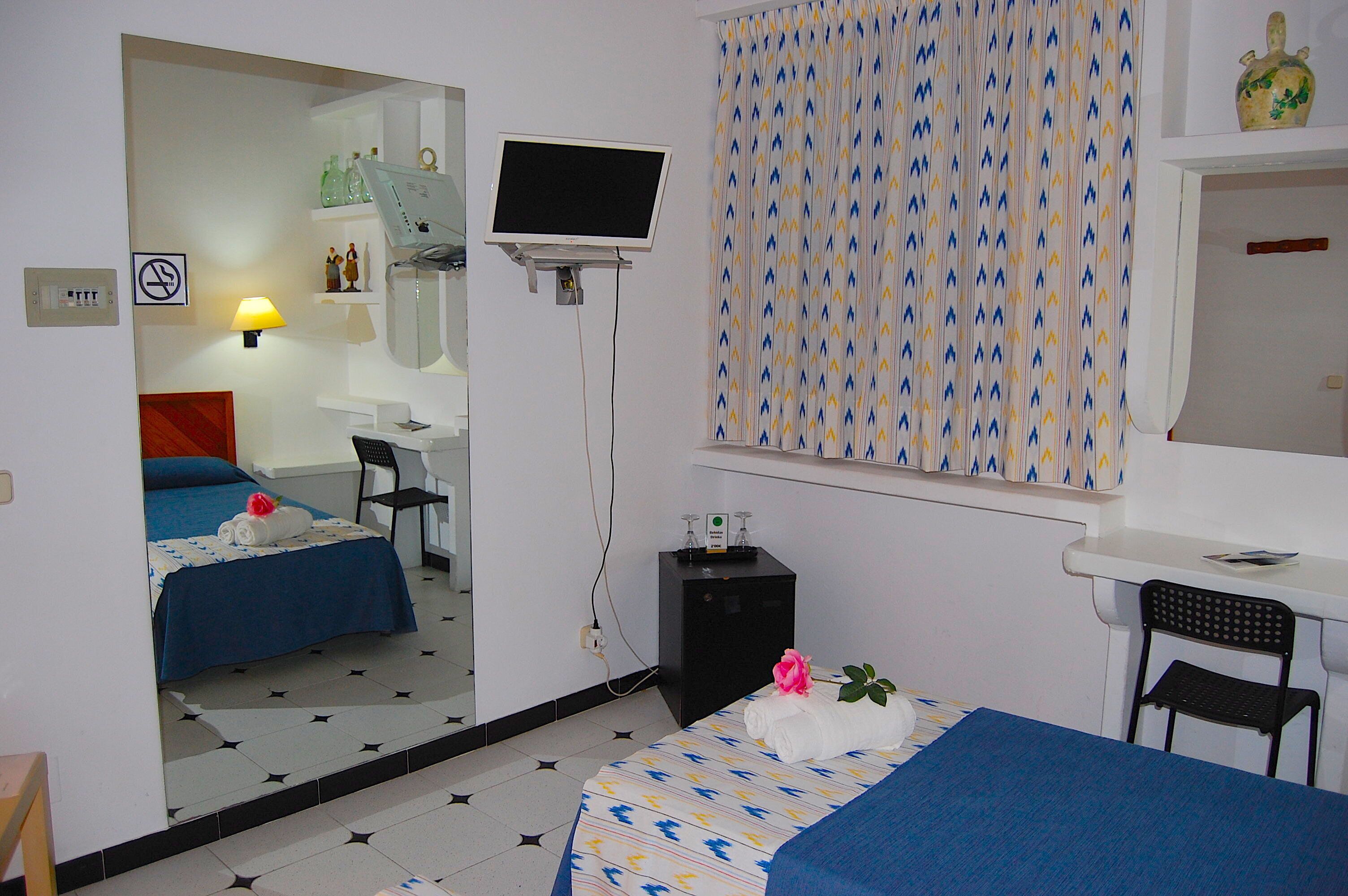 Una habitación de hotel con dos camas, un escritorio, una silla, un televisor y un espejo.