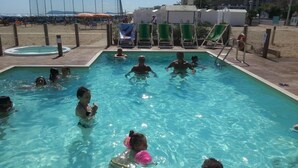 Una piscina con gente en el agua, rodeada de sillas de playa y sombrillas.