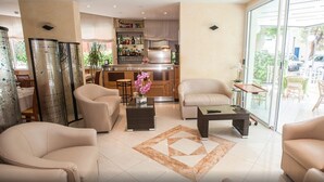 Una sala de estar moderna con una zona de bar, sofás beige y un ventanal que da a un patio exterior.