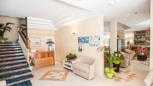 Un vestíbulo amplio con una escalera, una recepción y un área de descanso con sofás y plantas en macetas.